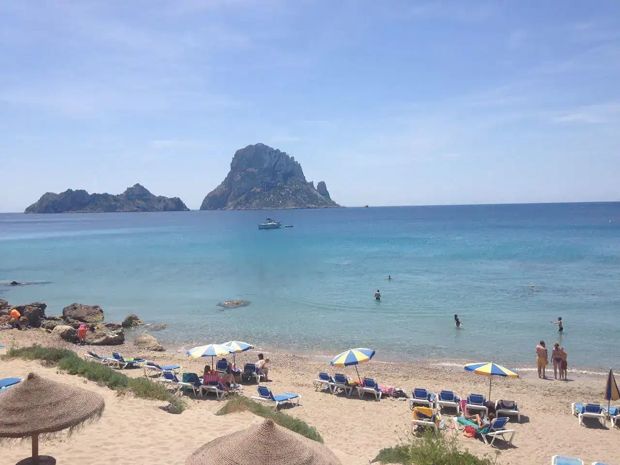 Ibiza beach with turquoise water, sandy shore, umbrellas, and Es Vedrà island view.