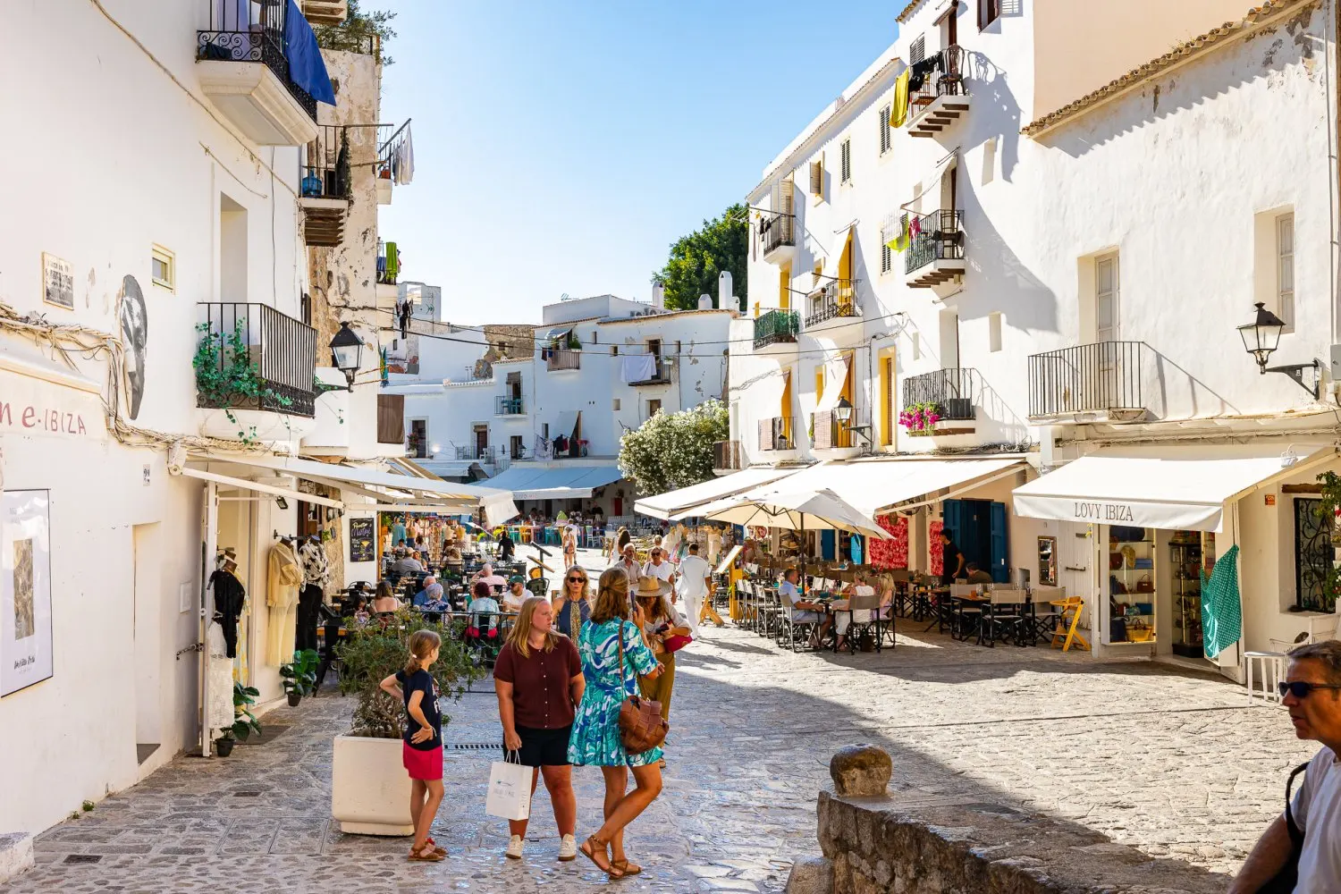 Ibiza old town street with white buildings, cafes, shops, and cobblestone paths.